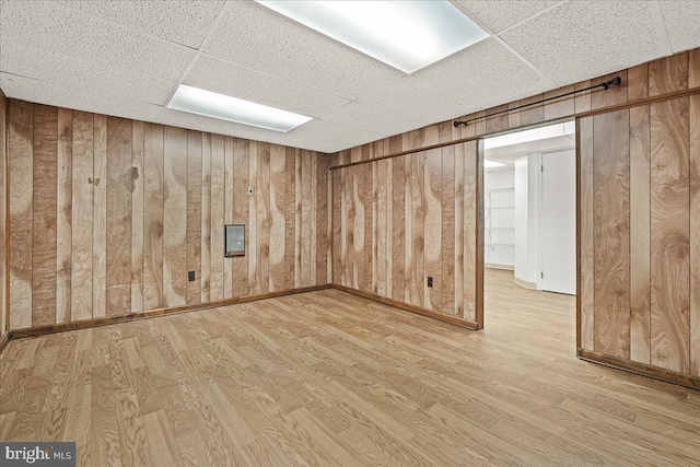 finished basement featuring wood finished floors, a paneled ceiling, and wooden walls