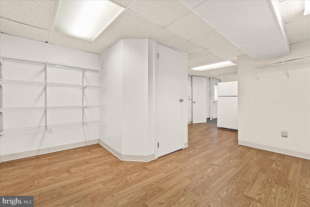 interior space with baseboards, a drop ceiling, wood finished floors, and freestanding refrigerator