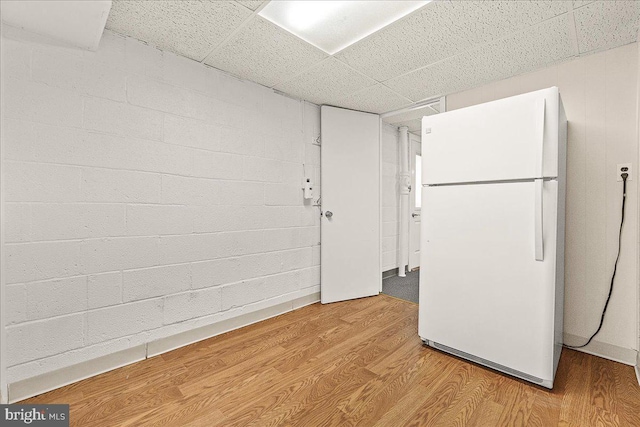 unfurnished room with a drop ceiling, wood finished floors, and concrete block wall