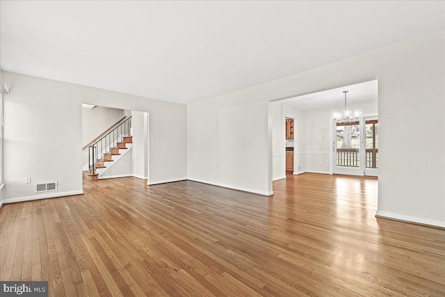 unfurnished living room with a notable chandelier, visible vents, stairway, wood finished floors, and baseboards