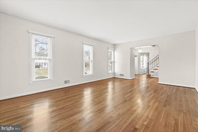 unfurnished living room with plenty of natural light, stairs, visible vents, and wood finished floors