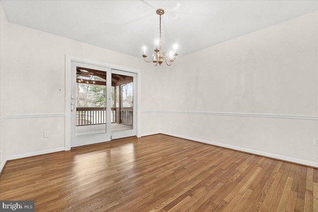 empty room with a chandelier, baseboards, and wood finished floors