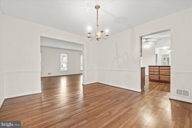 unfurnished room with hardwood / wood-style flooring, baseboards, visible vents, and ceiling fan with notable chandelier