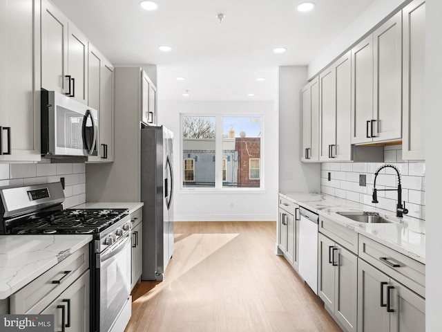 kitchen featuring sink, light stone counters, appliances with stainless steel finishes, light hardwood / wood-style floors, and decorative backsplash