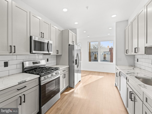 kitchen featuring light stone countertops, stainless steel appliances, sink, and light wood-type flooring