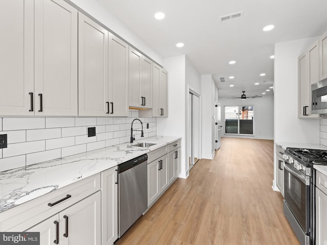 kitchen with sink, light stone counters, appliances with stainless steel finishes, decorative backsplash, and white cabinets