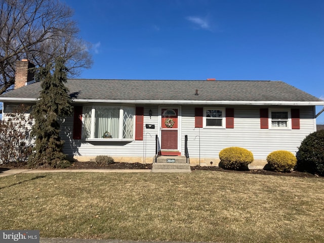 ranch-style home with entry steps, a front lawn, and roof with shingles