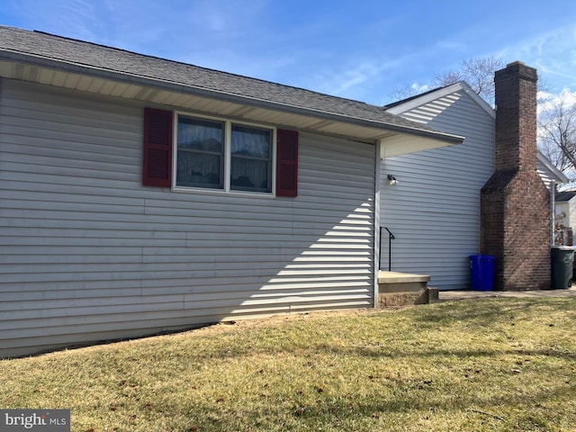 exterior space with roof with shingles, a front lawn, and a chimney