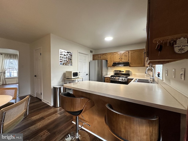 kitchen with appliances with stainless steel finishes, dark hardwood / wood-style floors, sink, a breakfast bar area, and kitchen peninsula