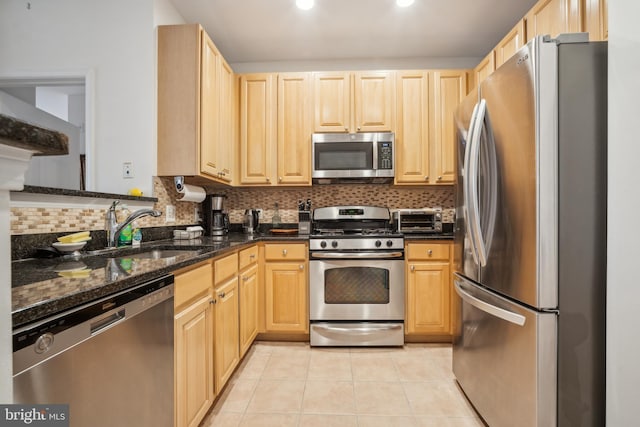 kitchen with sink, appliances with stainless steel finishes, dark stone countertops, light tile patterned flooring, and light brown cabinets