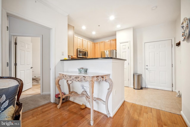 kitchen featuring stainless steel appliances, light brown cabinetry, kitchen peninsula, and light hardwood / wood-style flooring