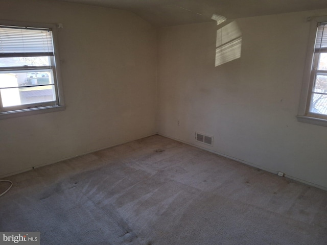 carpeted spare room with a wealth of natural light and vaulted ceiling