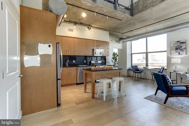 kitchen featuring a breakfast bar, stainless steel appliances, light hardwood / wood-style floors, decorative backsplash, and a high ceiling