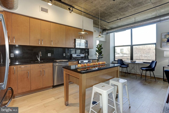 kitchen featuring appliances with stainless steel finishes, sink, backsplash, hanging light fixtures, and light wood-type flooring