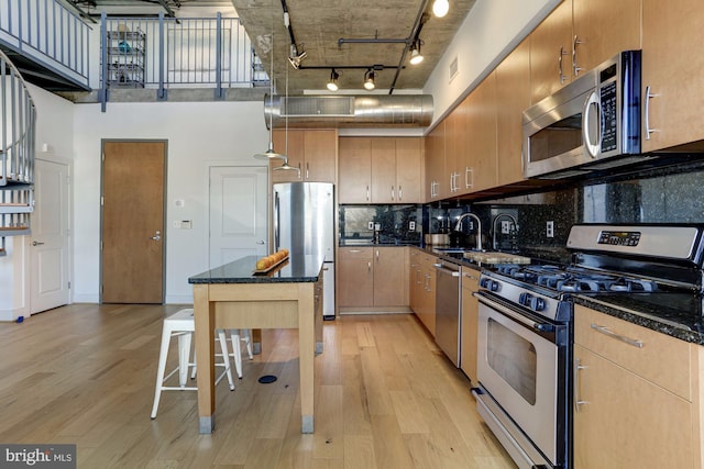 kitchen with appliances with stainless steel finishes, light hardwood / wood-style floors, a breakfast bar area, and dark stone countertops