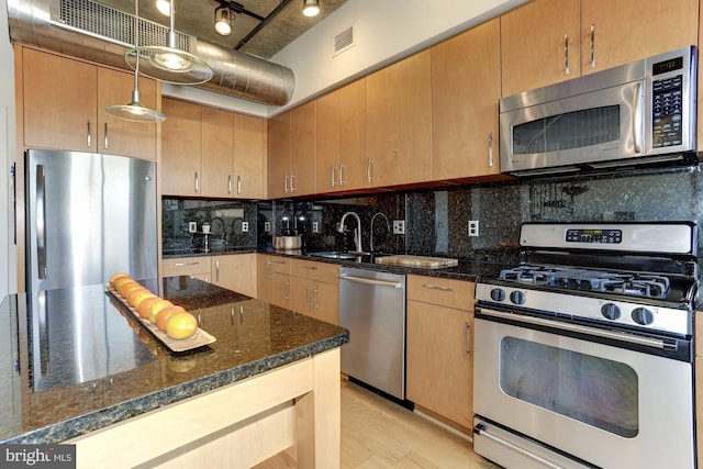 kitchen featuring appliances with stainless steel finishes, sink, dark stone countertops, decorative backsplash, and hanging light fixtures