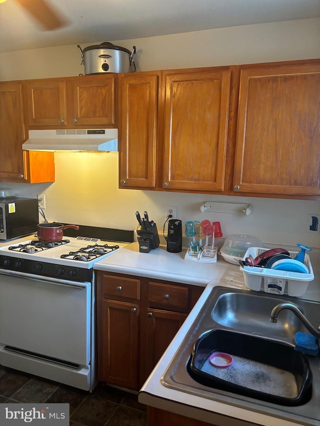 kitchen with white gas range, sink, and dark tile patterned floors