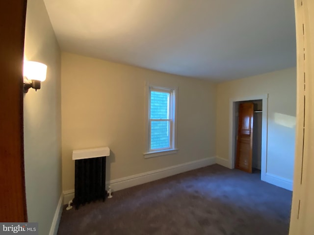 empty room featuring dark carpet and radiator heating unit