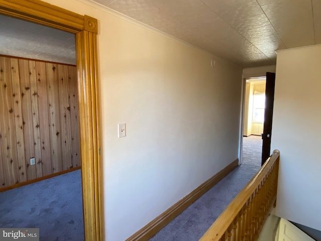 hall with carpet floors, ornamental molding, and wooden walls