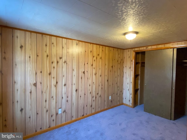 unfurnished bedroom with carpet, wooden walls, and a closet