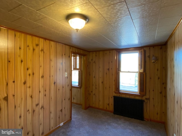 carpeted empty room featuring radiator heating unit and wood walls