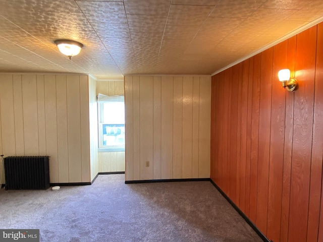 unfurnished room featuring radiator heating unit, wood walls, and carpet