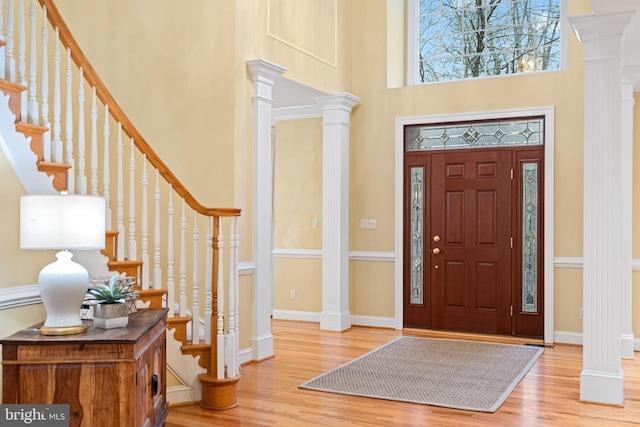 foyer entrance with a towering ceiling, light hardwood / wood-style floors, and ornate columns