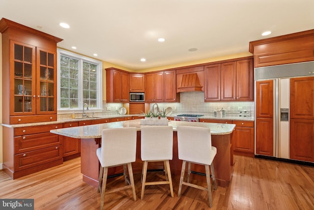 kitchen featuring built in appliances, sink, light stone counters, and a center island