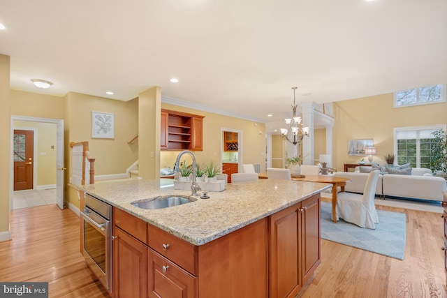 kitchen featuring sink, light stone counters, decorative light fixtures, a center island with sink, and oven