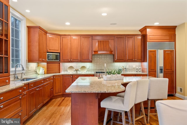 kitchen with a kitchen island, sink, custom exhaust hood, built in appliances, and light stone countertops