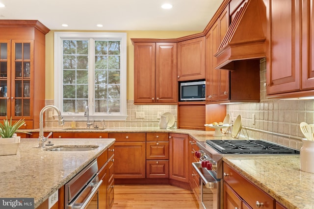 kitchen featuring premium range hood, appliances with stainless steel finishes, sink, light stone counters, and light hardwood / wood-style floors