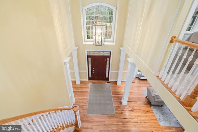 foyer featuring a towering ceiling, decorative columns, a chandelier, and light wood-type flooring