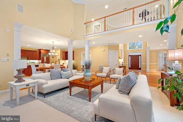 living room featuring an inviting chandelier, a towering ceiling, light hardwood / wood-style flooring, and ornate columns