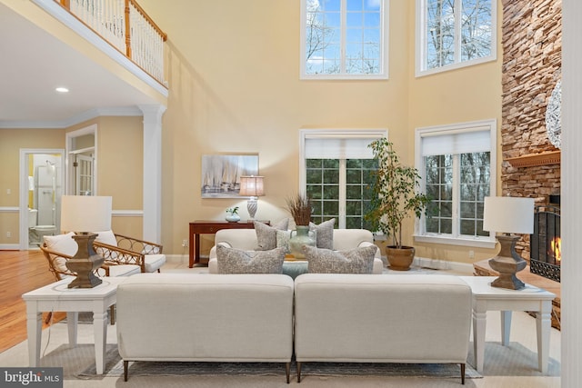 living room with ornate columns, a stone fireplace, hardwood / wood-style flooring, ornamental molding, and a high ceiling