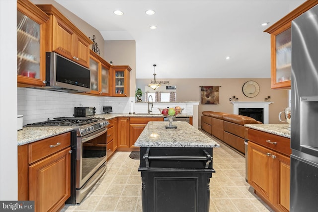 kitchen with pendant lighting, sink, stainless steel appliances, a center island, and light stone counters