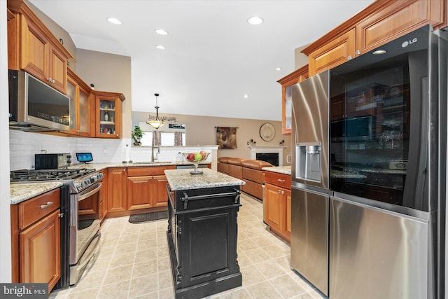 kitchen featuring a kitchen island, decorative light fixtures, sink, light stone counters, and stainless steel appliances