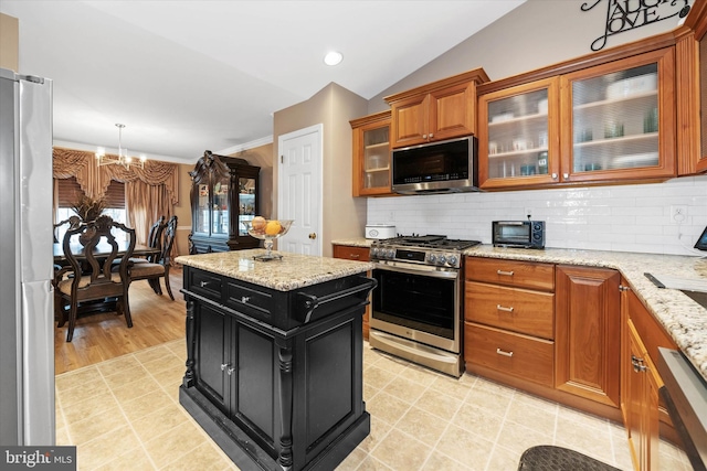 kitchen featuring lofted ceiling, appliances with stainless steel finishes, light stone countertops, and backsplash