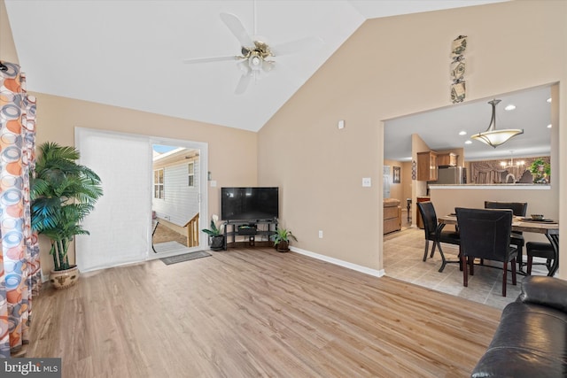 living room with ceiling fan with notable chandelier, high vaulted ceiling, and light hardwood / wood-style floors