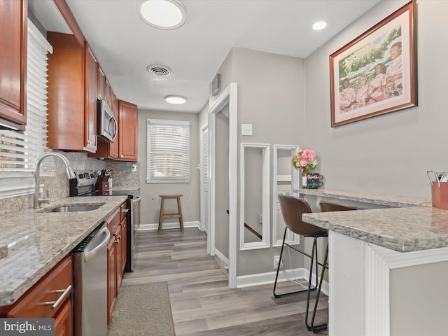 kitchen featuring appliances with stainless steel finishes, sink, a breakfast bar area, backsplash, and light stone counters