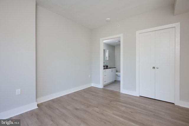 unfurnished bedroom featuring ensuite bath, light hardwood / wood-style flooring, and a closet