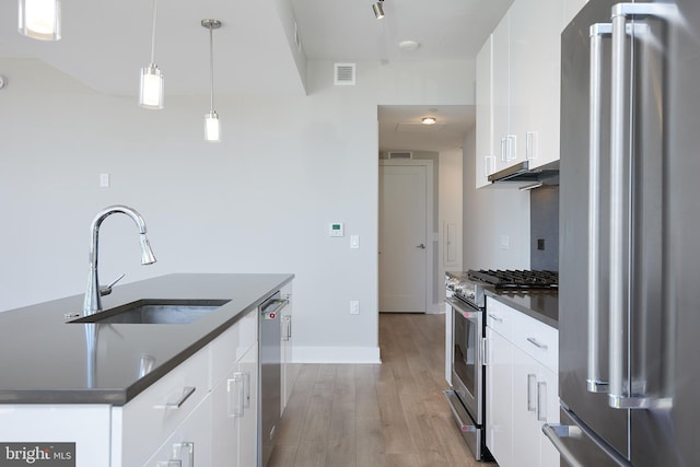 kitchen with appliances with stainless steel finishes, decorative light fixtures, white cabinetry, an island with sink, and sink