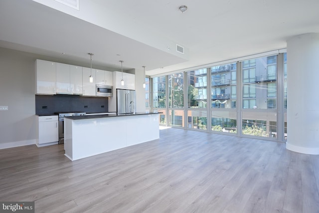 kitchen with pendant lighting, stainless steel appliances, floor to ceiling windows, white cabinets, and a center island with sink