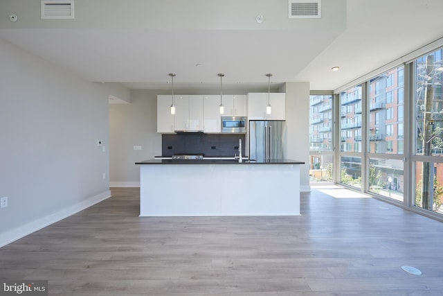 kitchen featuring appliances with stainless steel finishes, white cabinetry, decorative backsplash, hanging light fixtures, and expansive windows