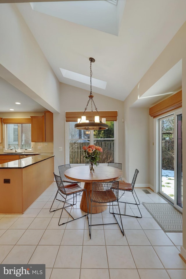 dining area featuring vaulted ceiling with skylight, sink, light tile patterned floors, and an inviting chandelier