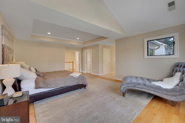 bedroom featuring vaulted ceiling, light hardwood / wood-style floors, and a raised ceiling