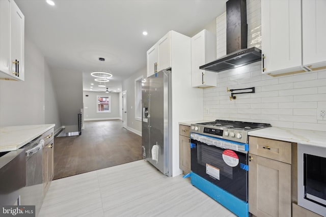 kitchen with wall chimney range hood, stainless steel appliances, light stone countertops, white cabinets, and decorative backsplash