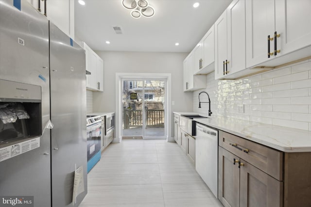 kitchen with sink, white cabinetry, tasteful backsplash, appliances with stainless steel finishes, and light stone countertops