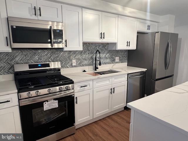 kitchen with sink, appliances with stainless steel finishes, white cabinetry, light stone countertops, and decorative backsplash