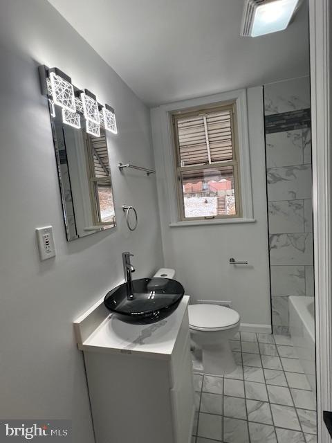 full bathroom featuring vanity, tiled shower / bath, and toilet