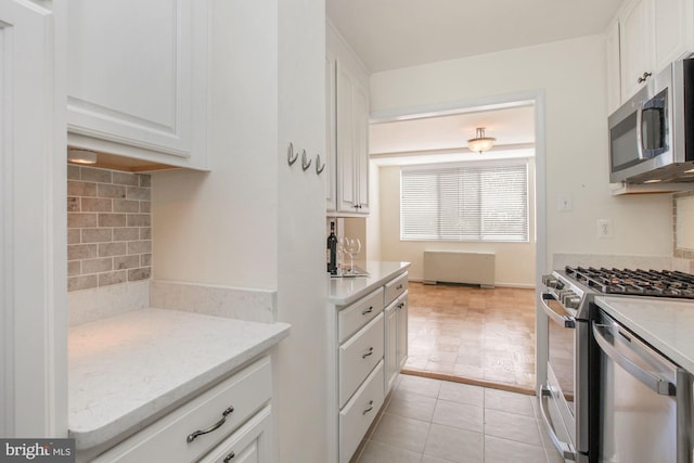 kitchen featuring appliances with stainless steel finishes, white cabinetry, backsplash, light tile patterned floors, and light stone counters